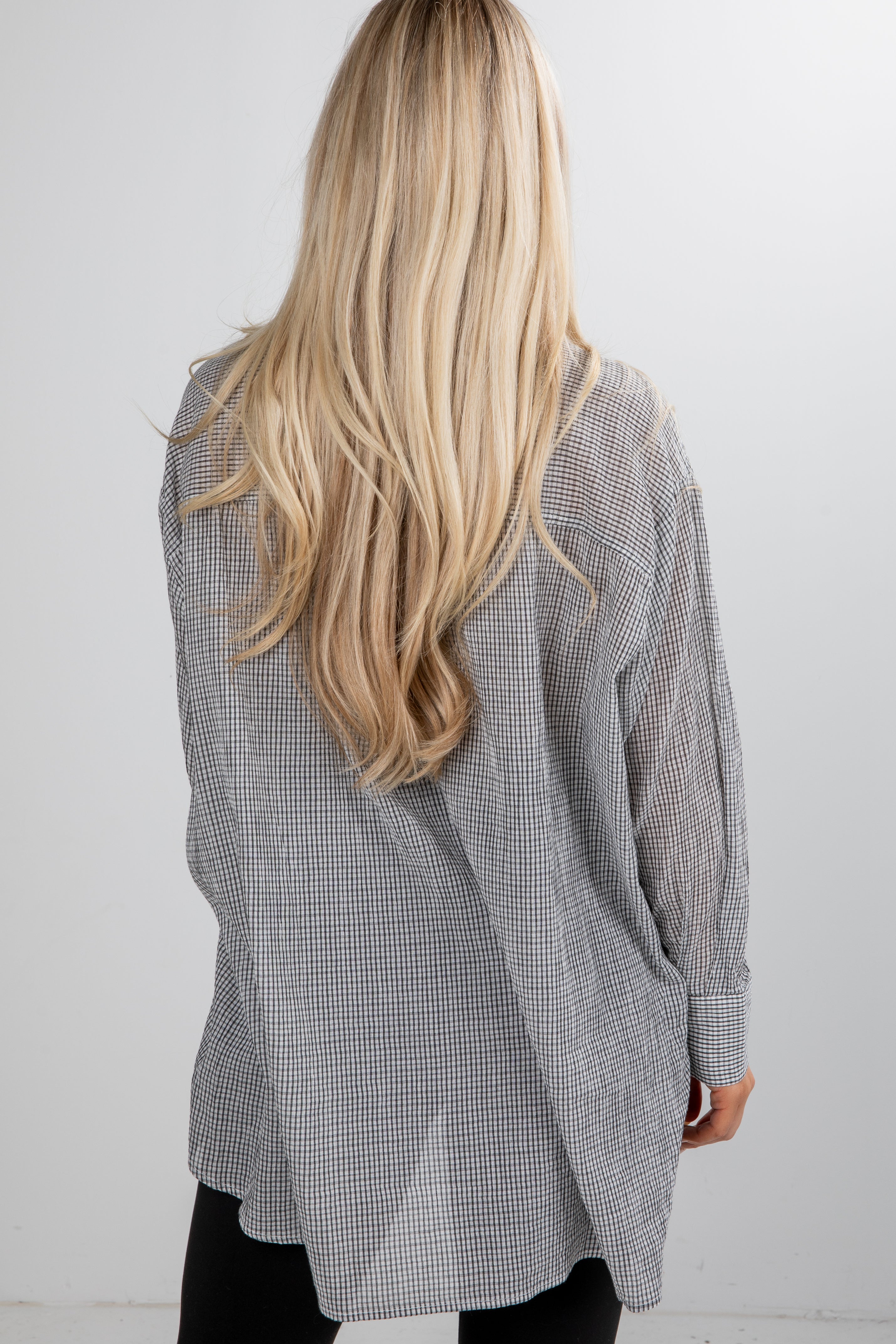 Person wearing a gray checkered shirt with long blonde hair, standing against a white background