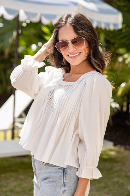 Woman wearing a white blouse and sunglasses outdoors with greenery in the background