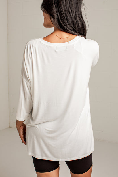 A woman shown from the back wearing a loose white long-sleeve t-shirt and black bike shorts against a light gray studio wall.