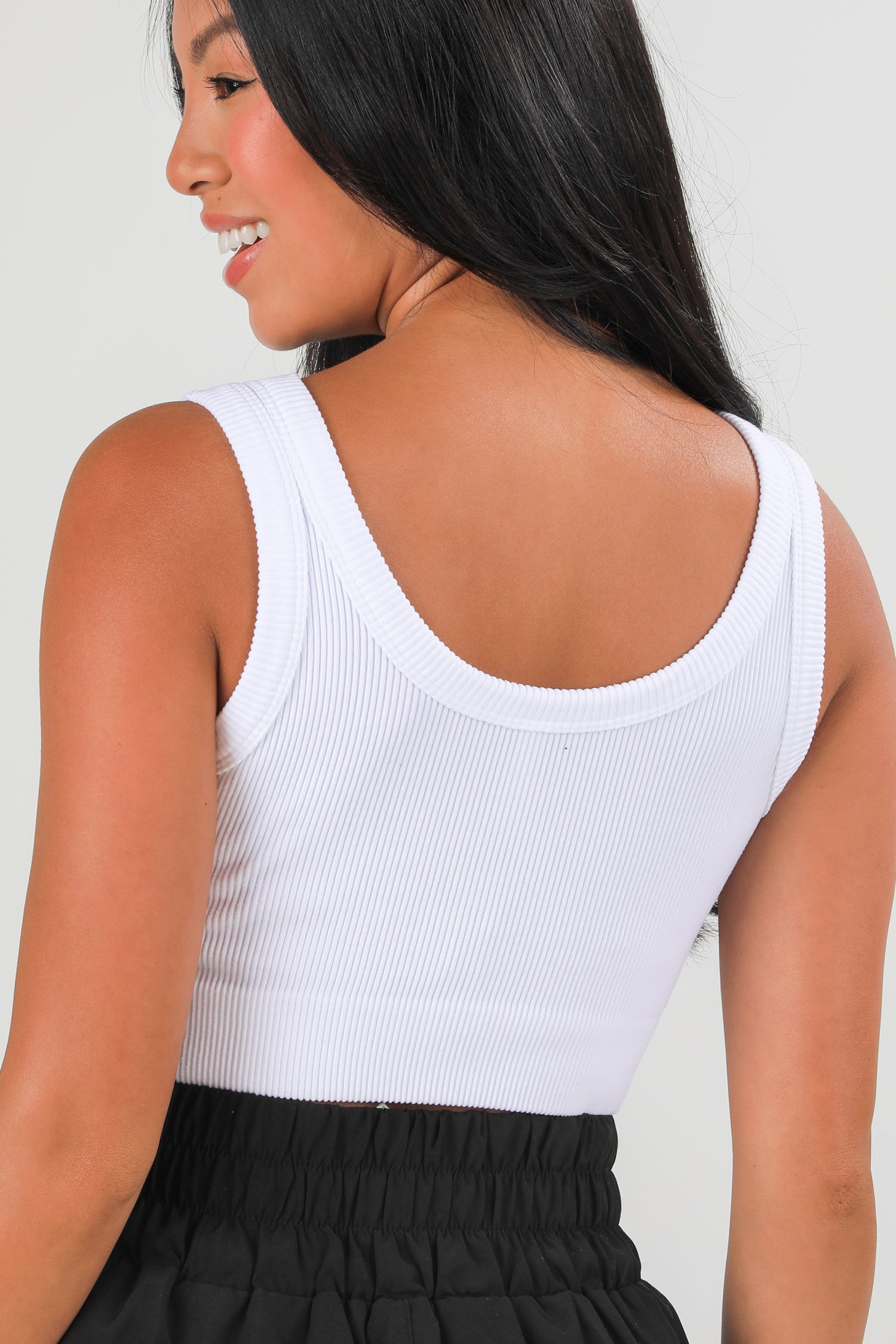 Woman wearing a white tank top and black skirt against a plain background