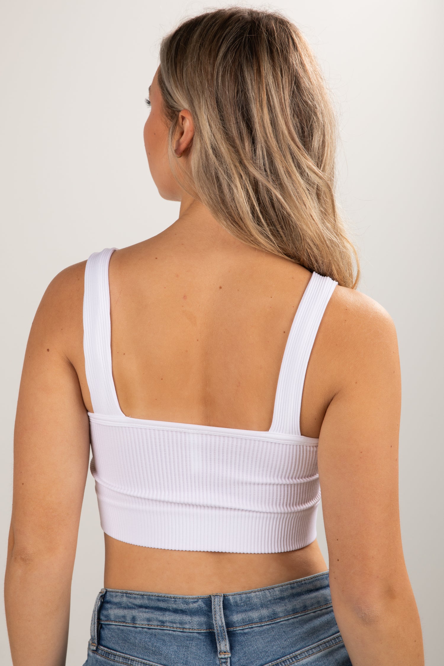 Person wearing a white ribbed crop top and blue jeans against a plain background