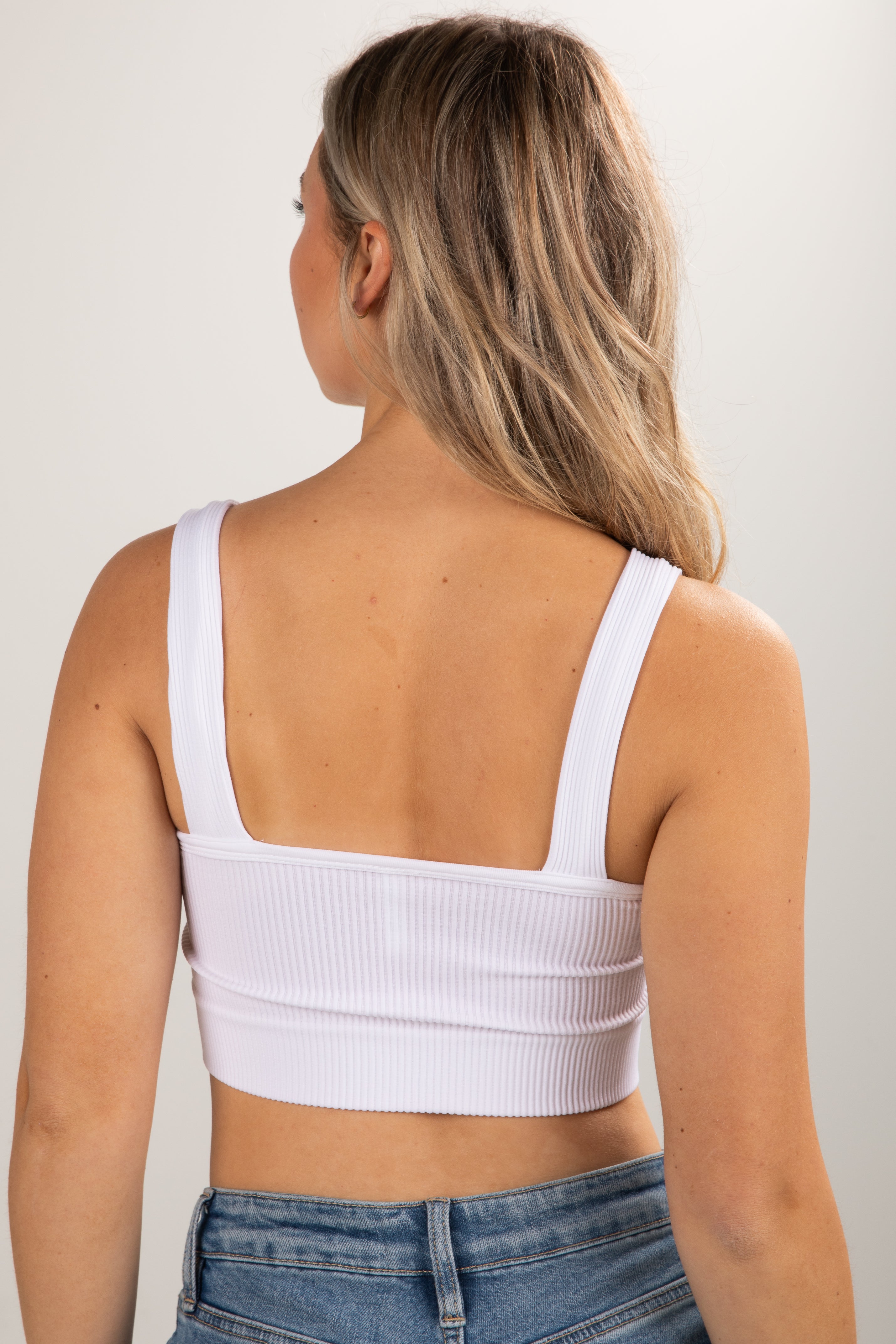 Person wearing a white ribbed crop top and blue jeans against a plain background