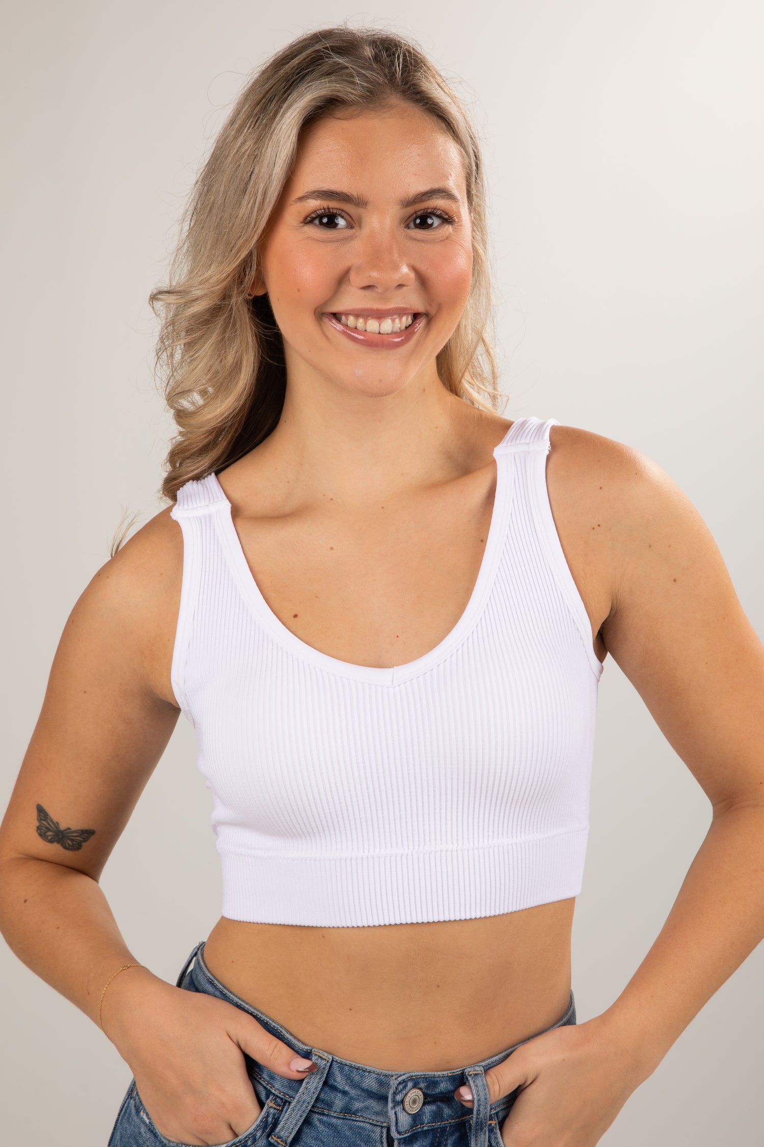 Woman wearing a white tank top against a plain background