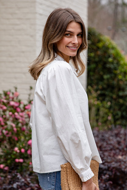Woman wearing a white blouse standing outdoors with flowers and a building in the background