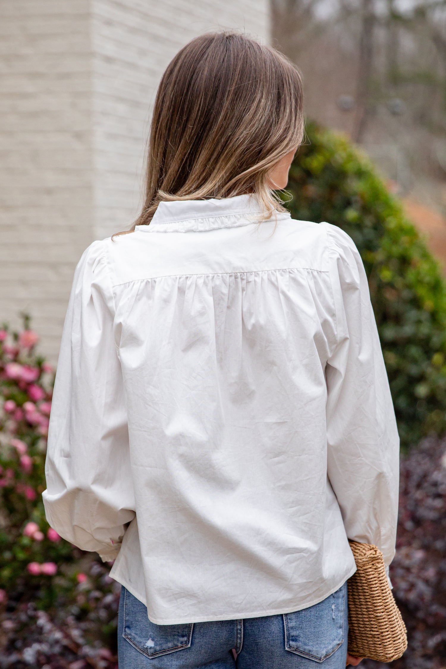Woman wearing a light-colored blouse and blue jeans, standing outdoors with blurred background