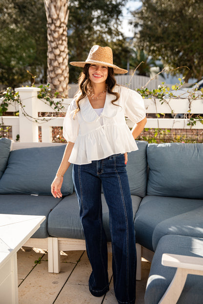 Woman in a white blouse and blue jeans standing on a patio with a blue sofa and white coffee table.