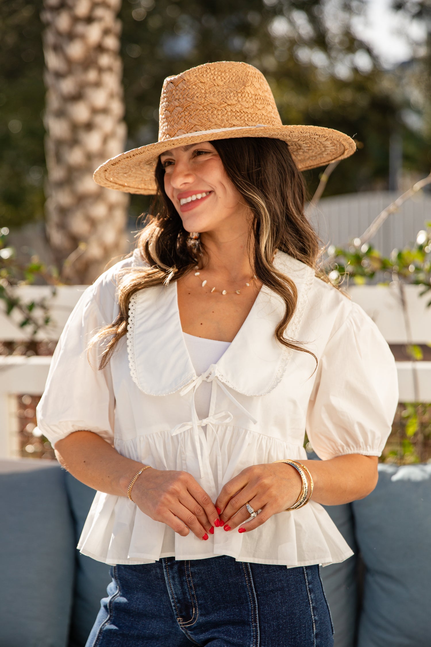 Woman wearing a white blouse, blue jeans, and a straw hat outdoors.