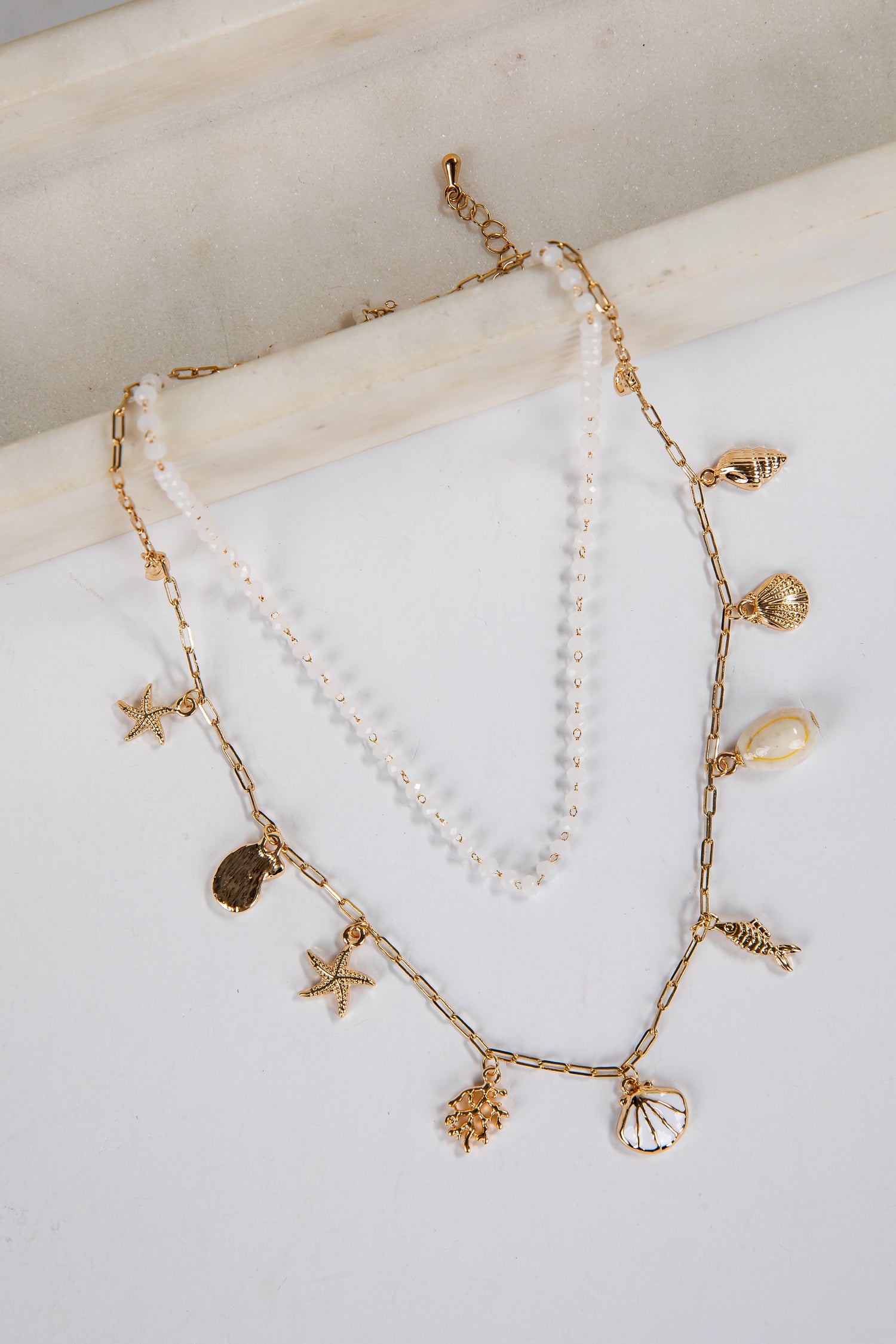 Two gold necklaces with starfish, shell, and pearl charms on a white surface.