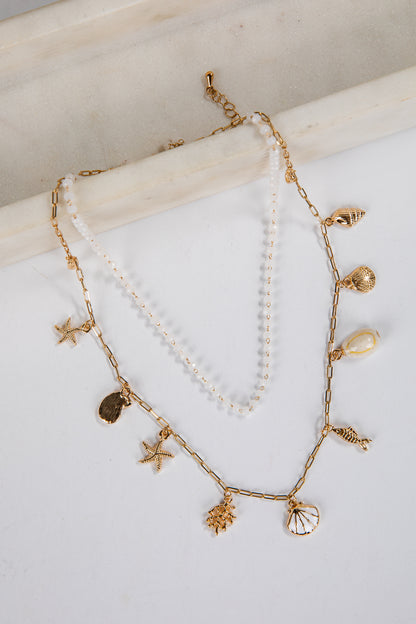 Two gold necklaces with starfish, shell, and pearl charms on a white surface.