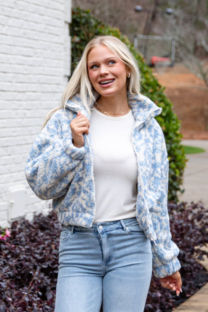 Woman wearing a blue floral jacket, white shirt, and jeans standing outdoors.
