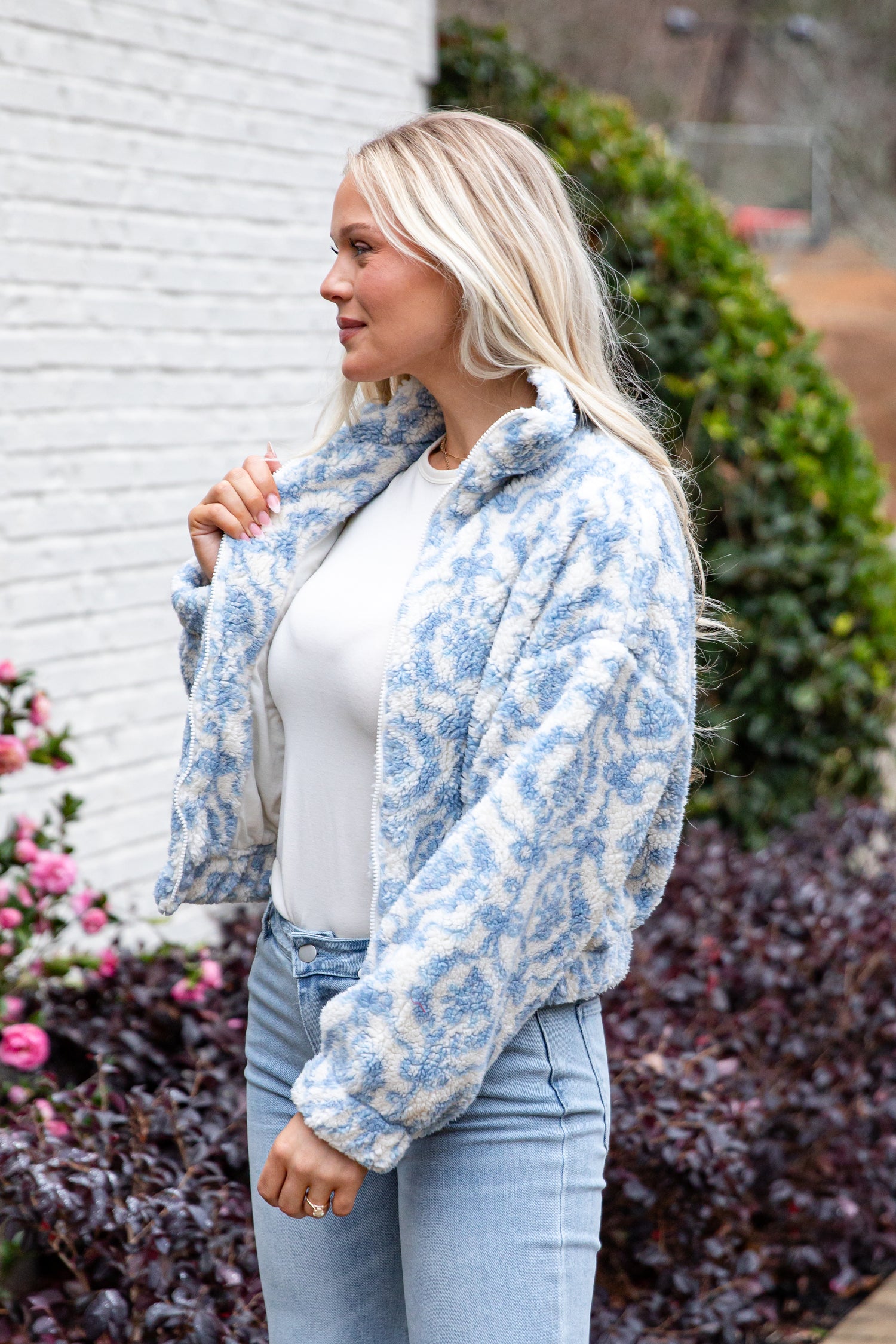 Woman wearing a blue floral jacket over a white top and light blue jeans, standing outdoors.