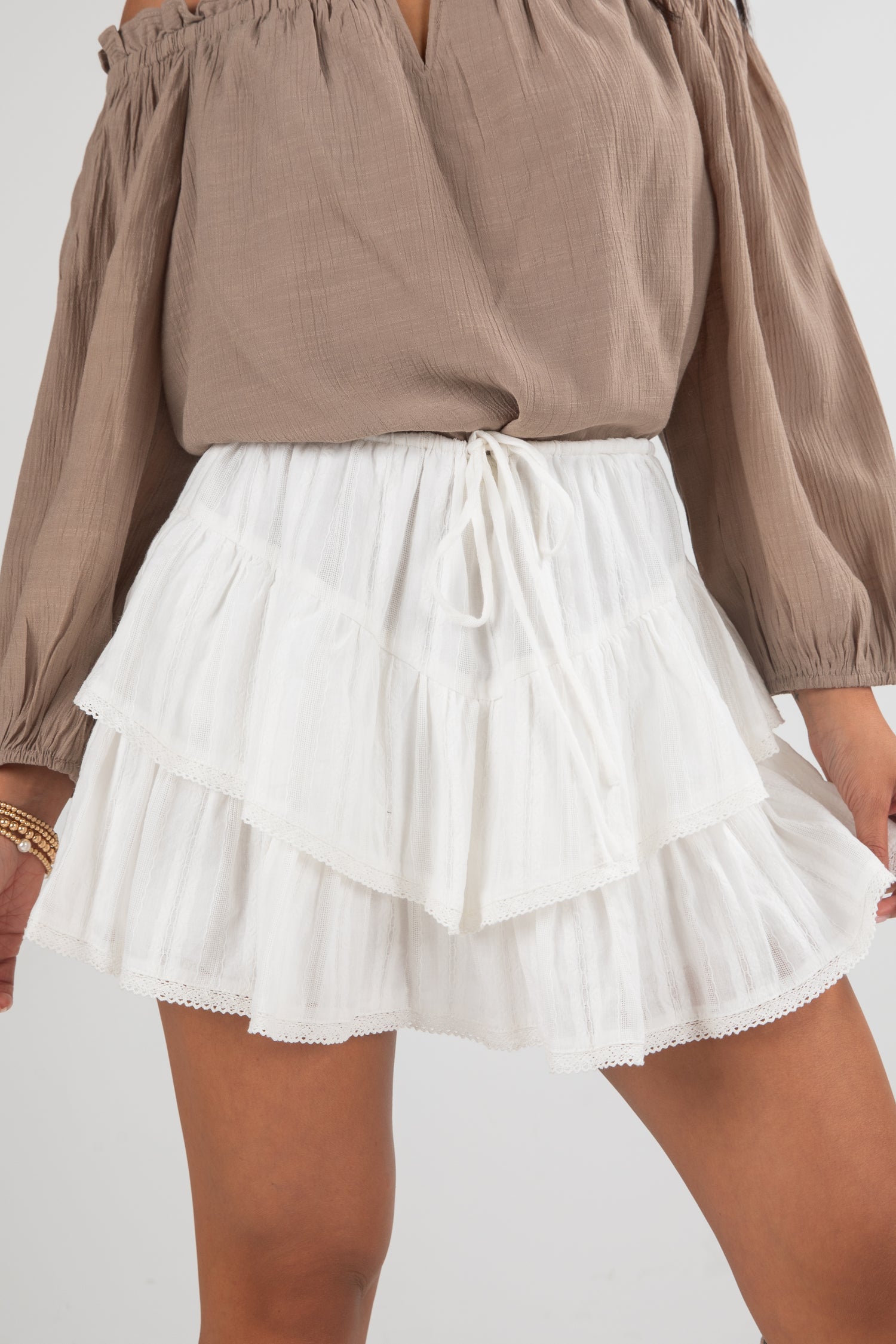 Brown off-shoulder top and white tiered skirt on a plain background