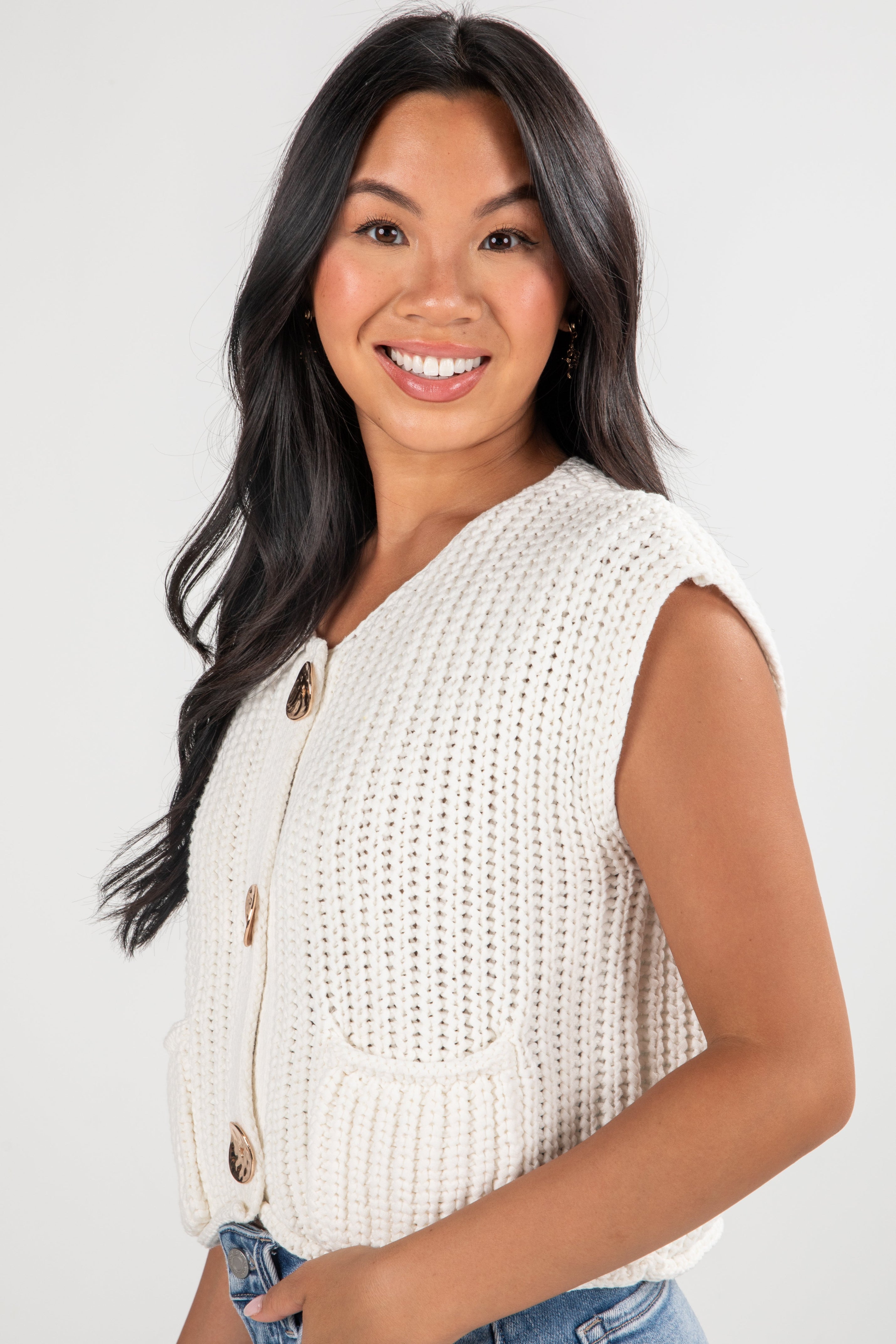Woman wearing a white sleeveless knitted cardigan on a plain background