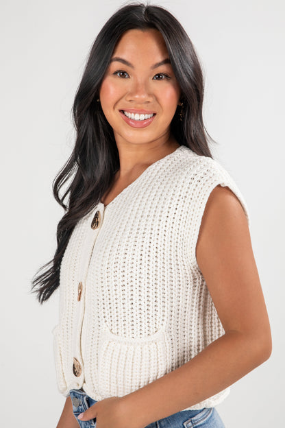 Woman wearing a white sleeveless knitted cardigan on a plain background