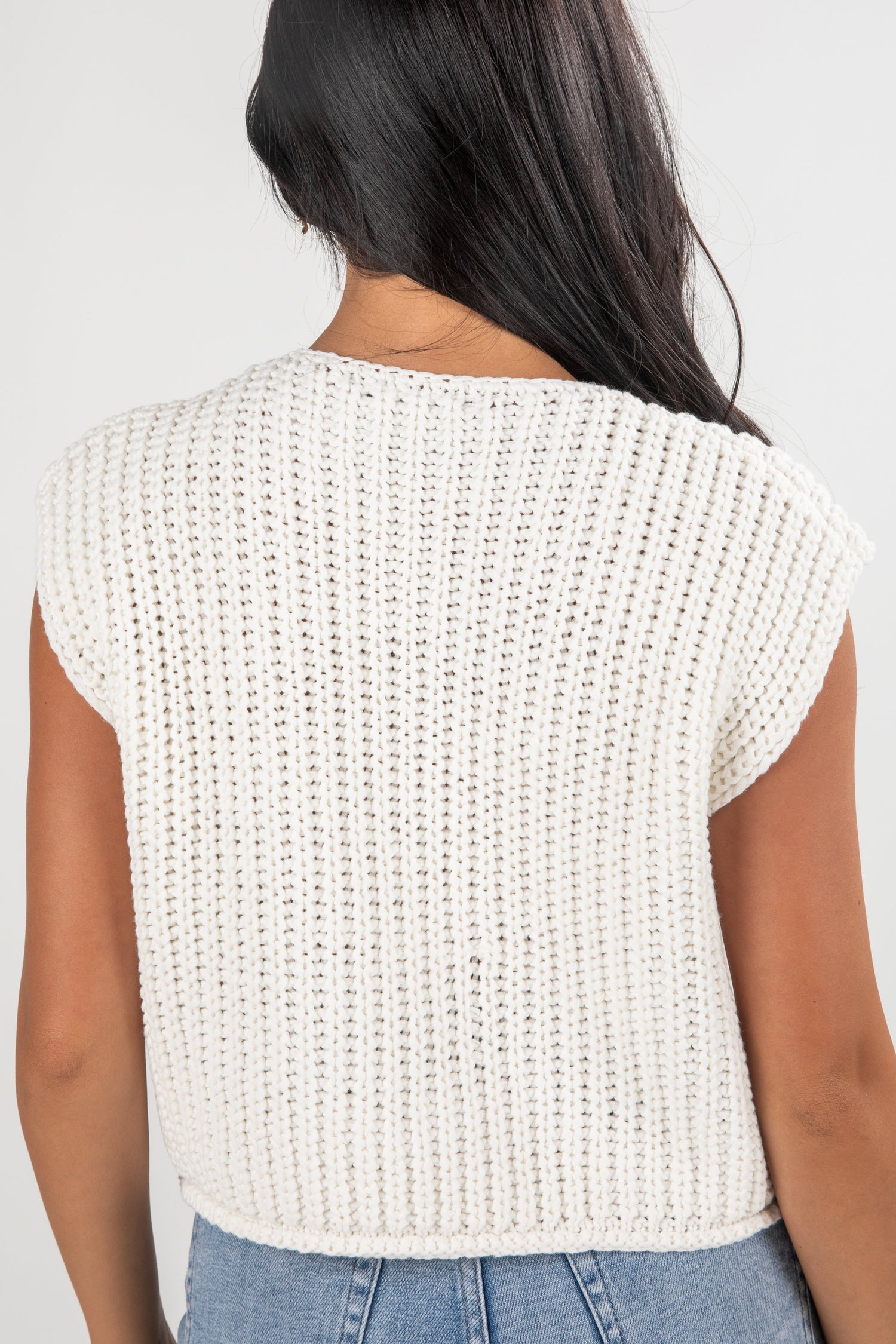 Person wearing a white knitted top with a plain background