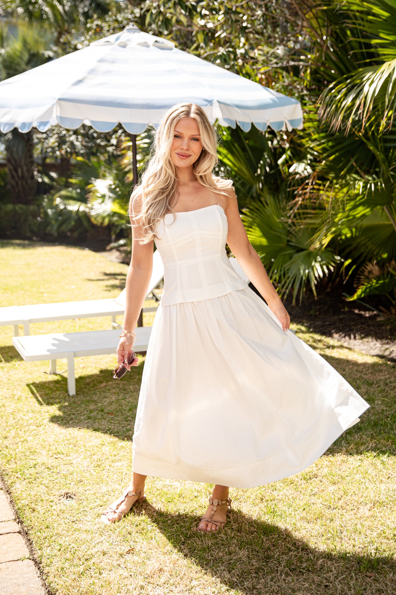 Woman in a white dress standing outdoors under a white umbrella with greenery in the background