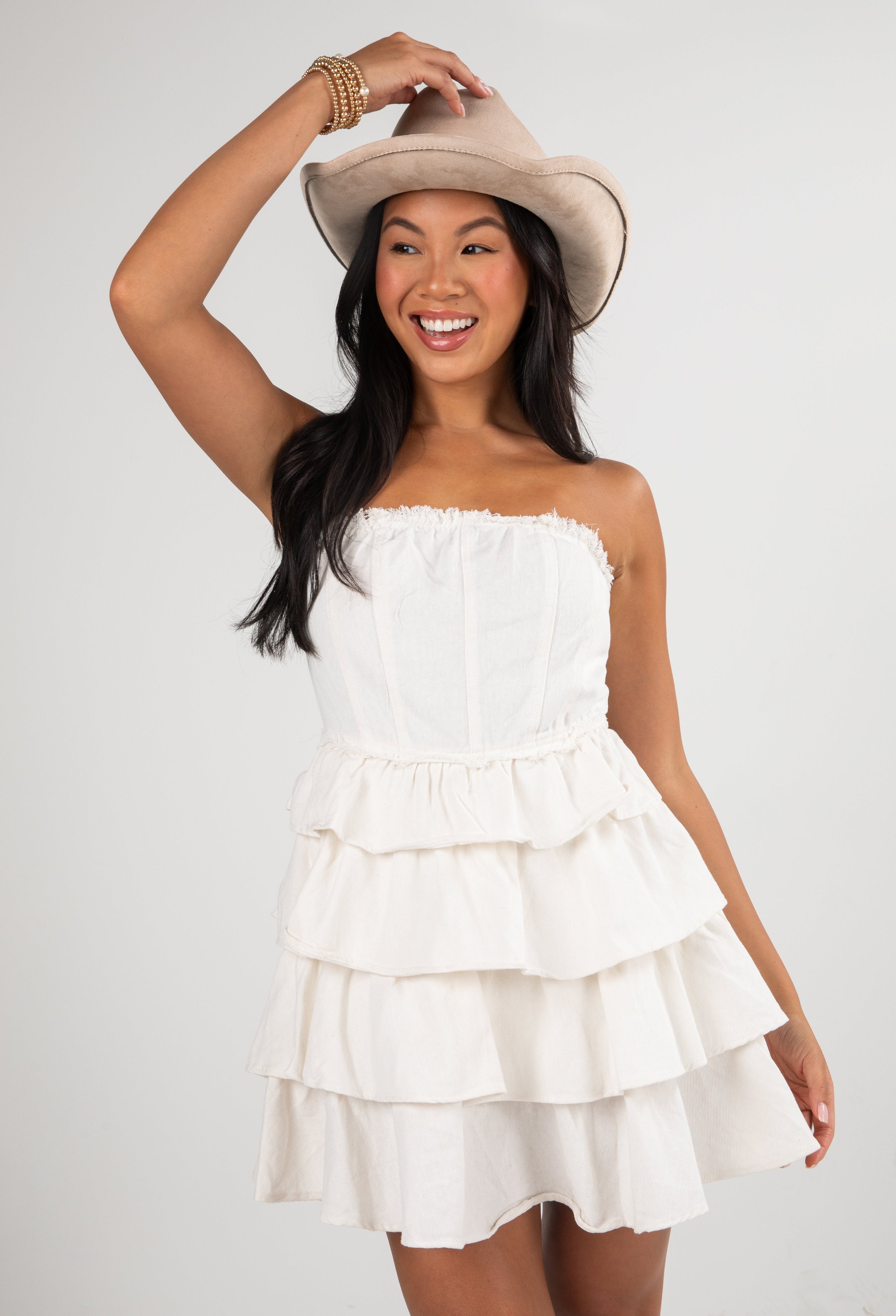 Woman wearing a white strapless dress and beige hat on a plain background