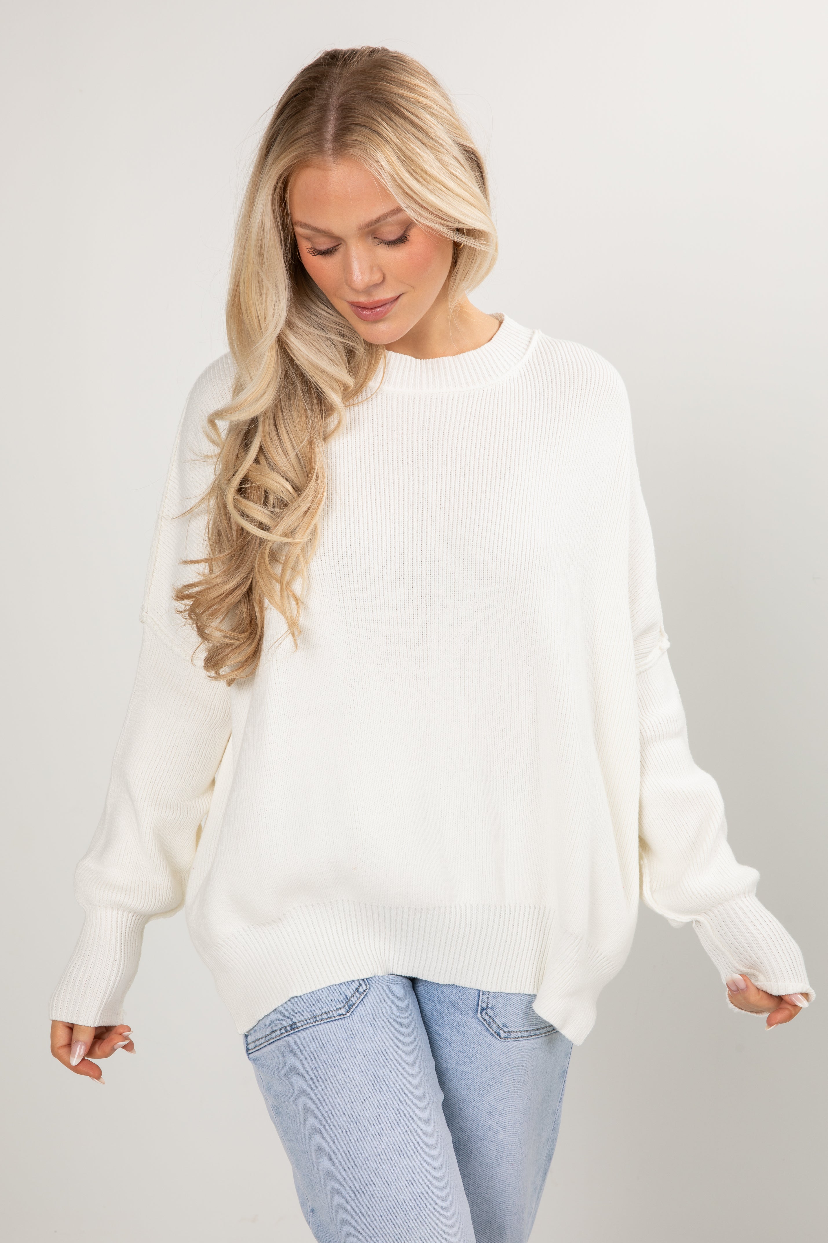 Woman wearing a white sweater and light blue jeans on a plain background
