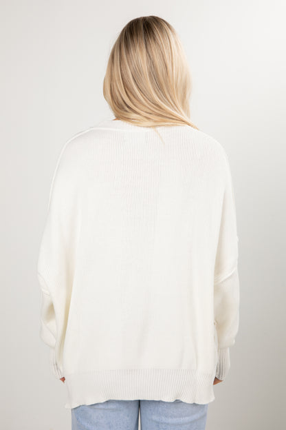 Person wearing a white sweater and light blue jeans on a plain background