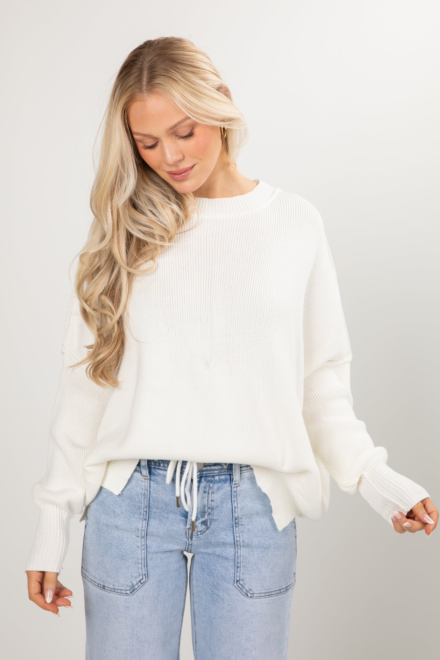 Woman wearing a white sweater and light blue jeans on a plain background