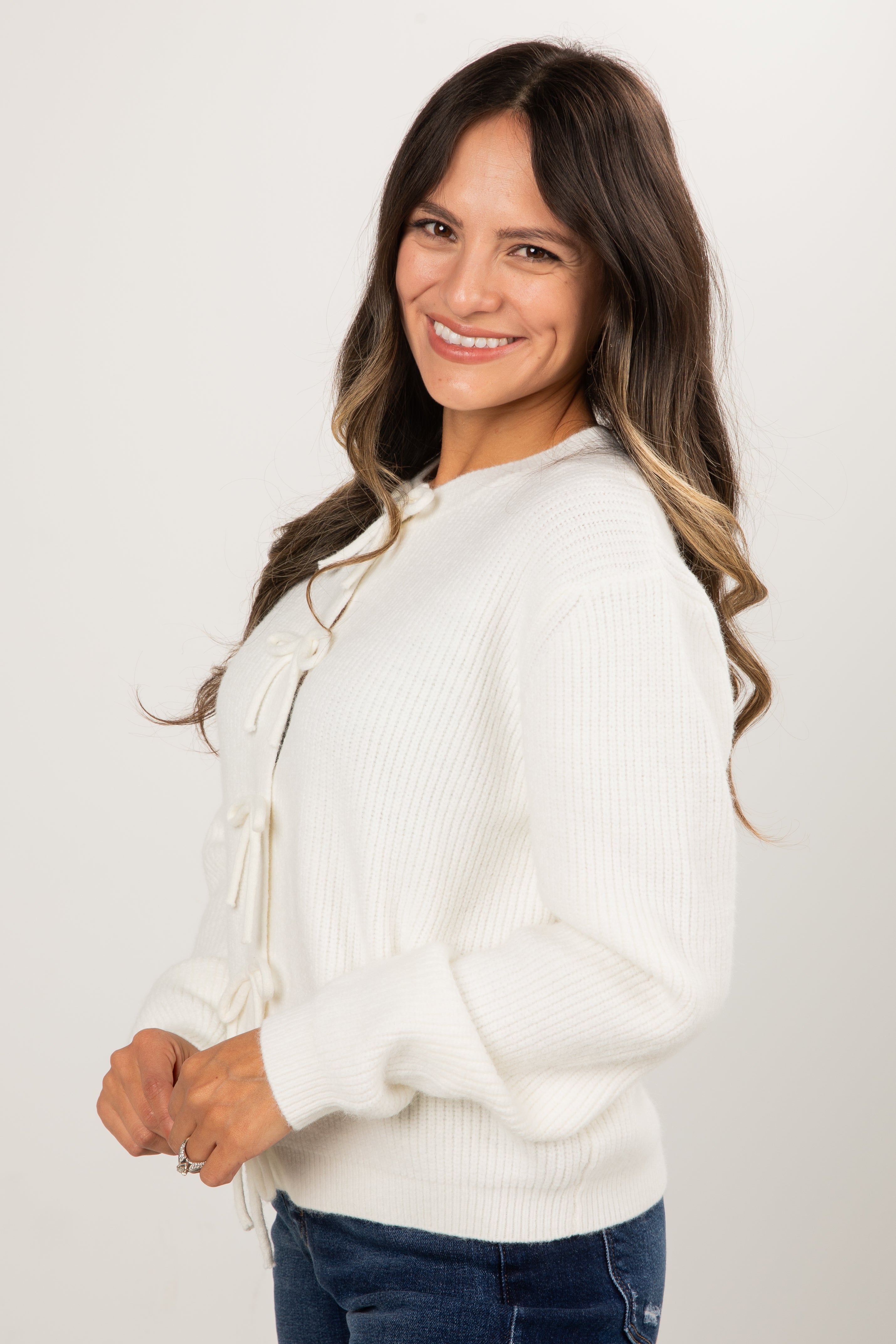 Woman wearing a white sweater and blue jeans against a plain background