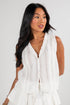 Woman wearing a white sleeveless dress with ruffled layers on a plain background