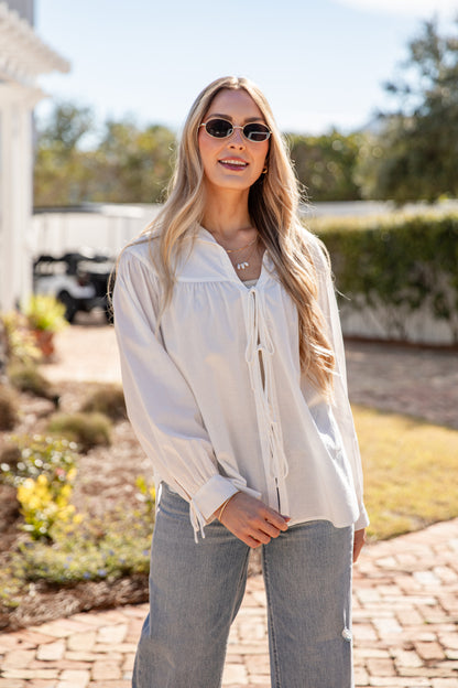 Woman wearing a white blouse and sunglasses outdoors.