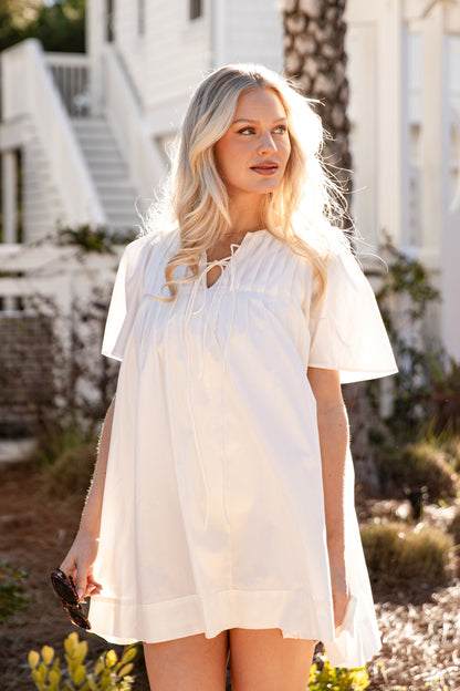 Woman in a white dress standing outdoors with a white building in the background