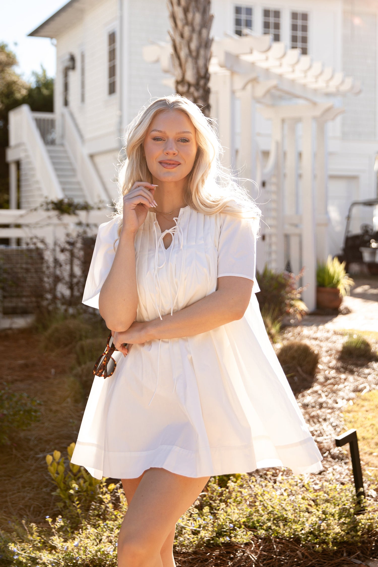 Woman in a white dress standing in front of a white house with a garden.