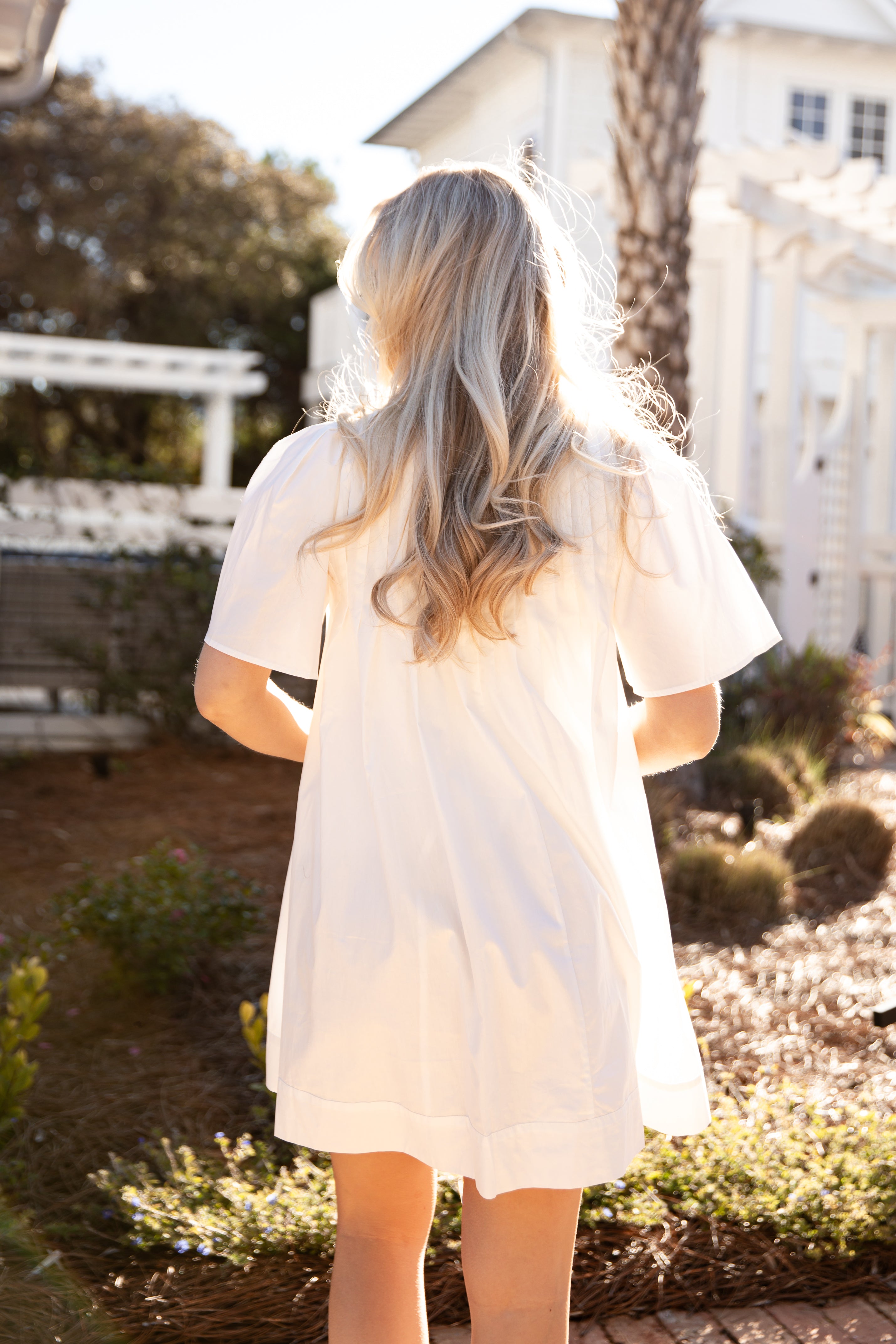 Person wearing a white dress with sheer sleeves in a garden setting