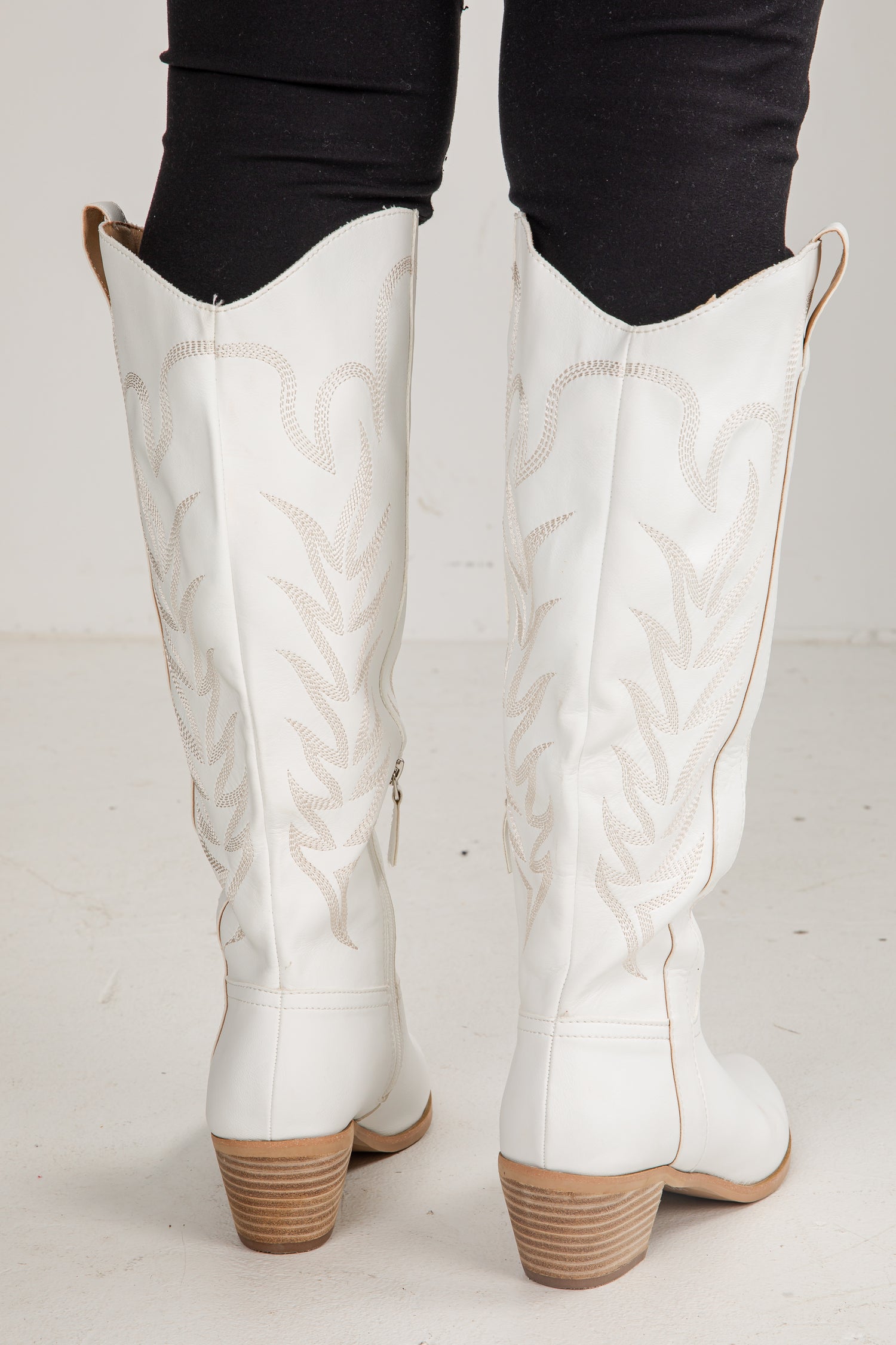 White knee-high boots with brown soles worn by a person on a light gray background