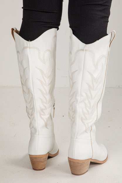 White knee-high boots with brown soles worn by a person on a light gray background