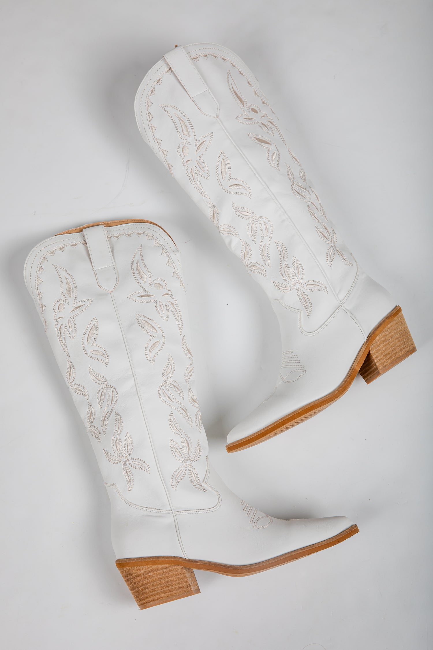 White cowboy boots with brown soles on a light gray background