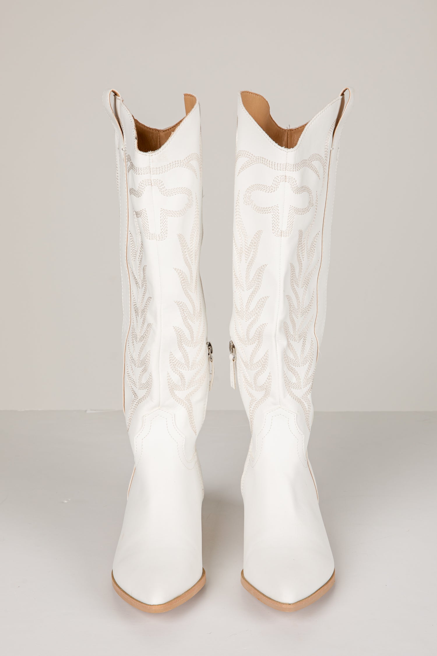 White cowboy boots with intricate detailing on a light gray background