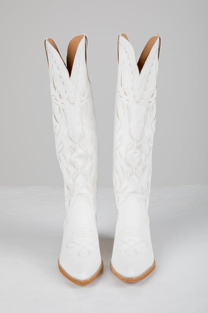 Pair of white cowboy boots with brown soles on a light gray background