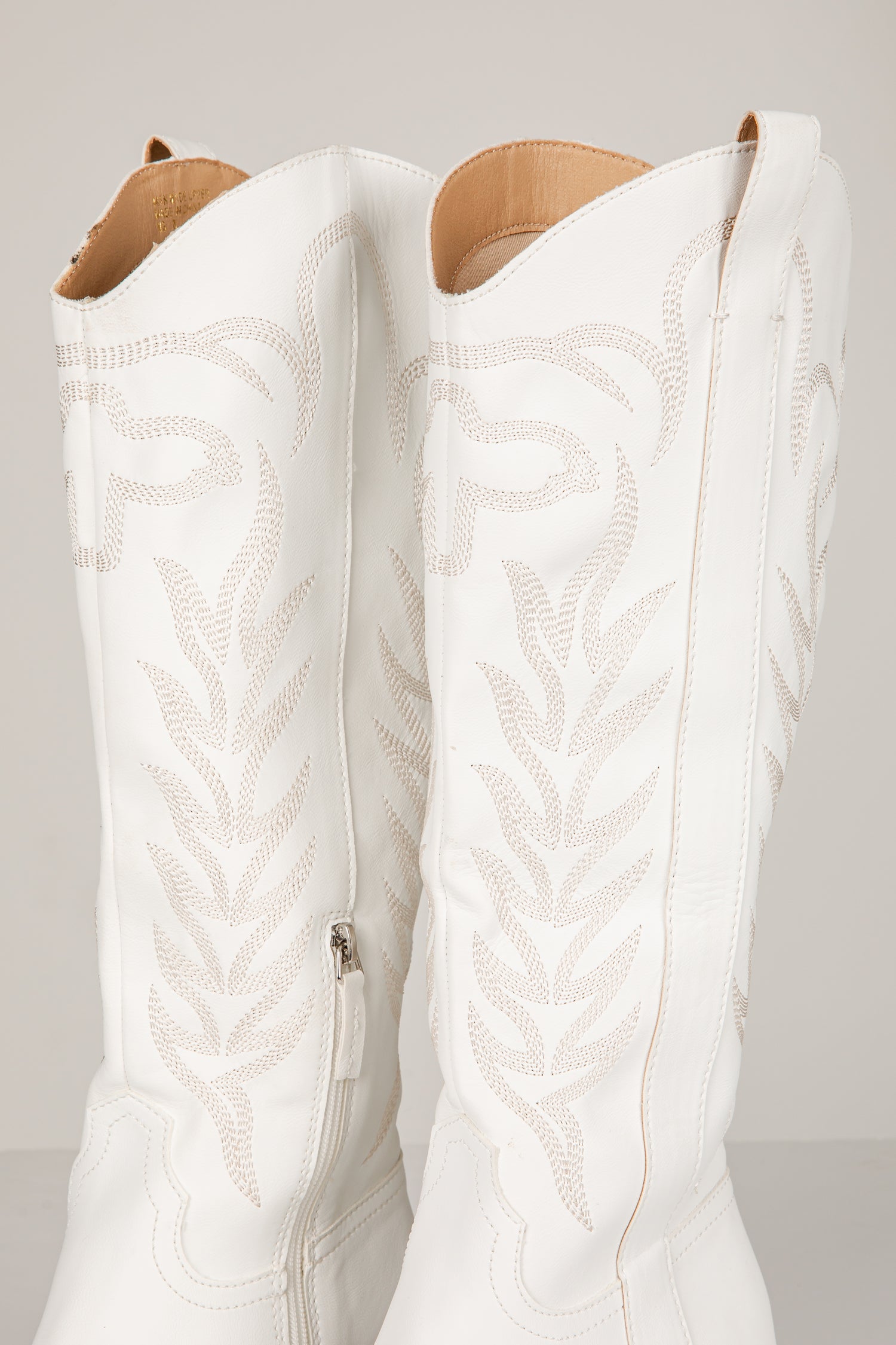 White cowboy boots with intricate patterns on a light gray background