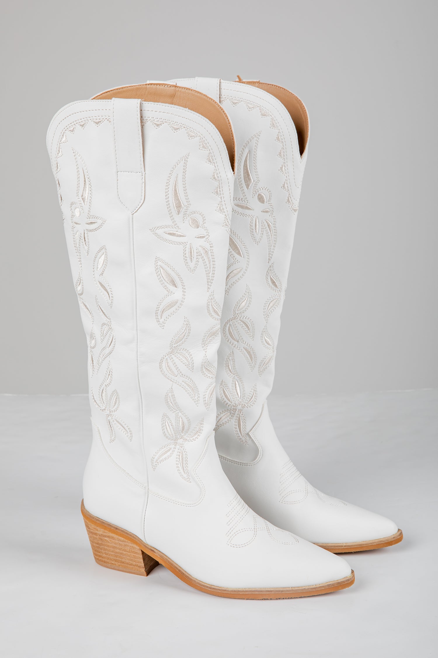 Pair of white cowboy boots with brown soles on a gray background