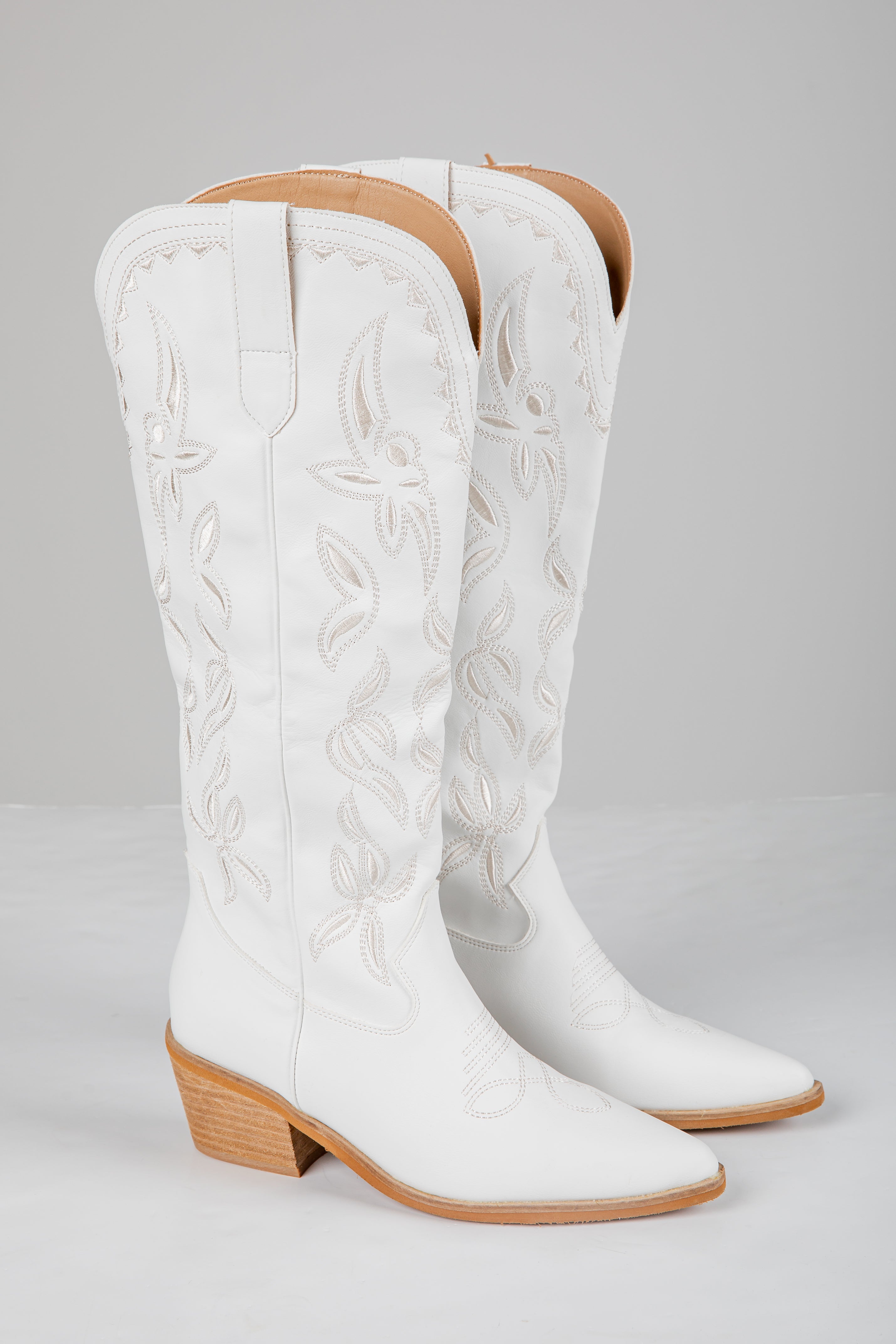 Pair of white cowboy boots with brown soles on a gray background