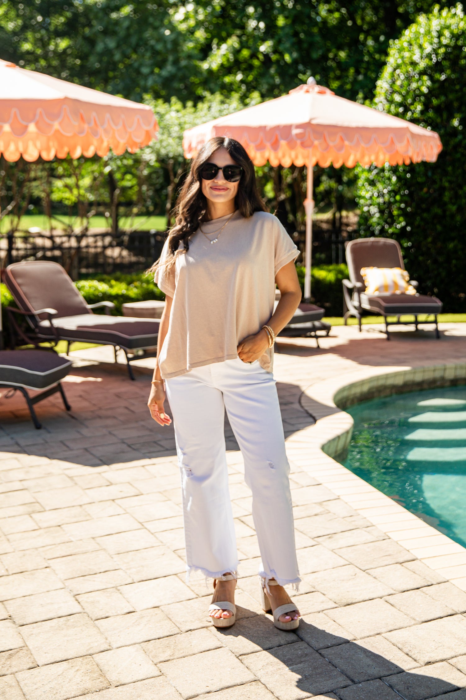 Woman standing by a pool with orange umbrellas and lounge chairs in the background