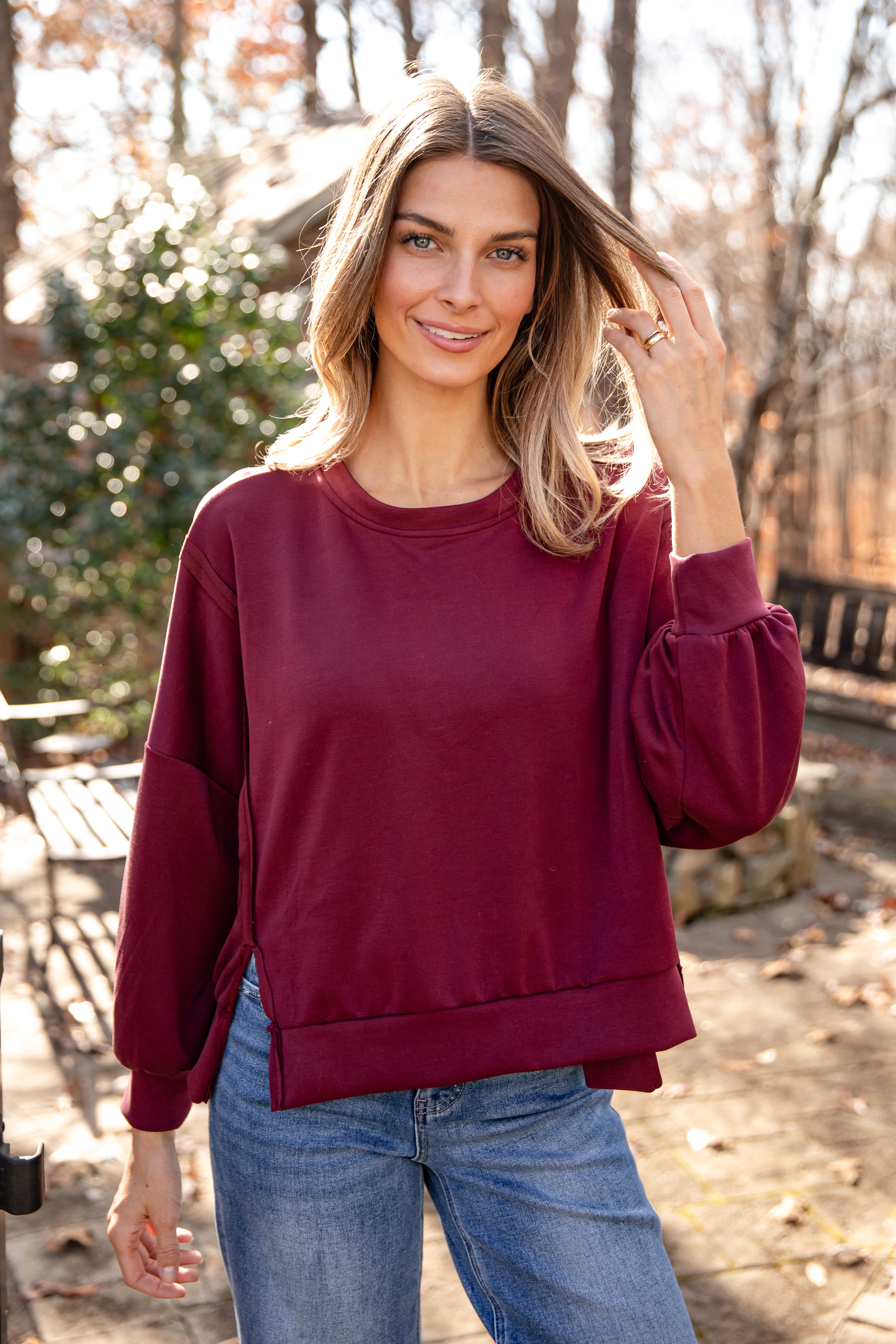 Woman wearing a maroon sweatshirt and blue jeans outdoors