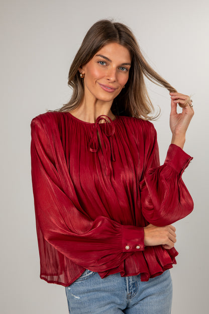 Woman wearing a red blouse with long sleeves and blue jeans on a plain background