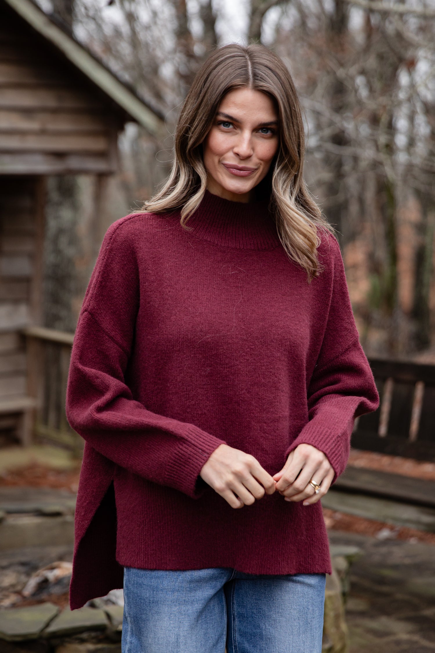 Woman wearing a maroon sweater outdoors with a wooden cabin in the background