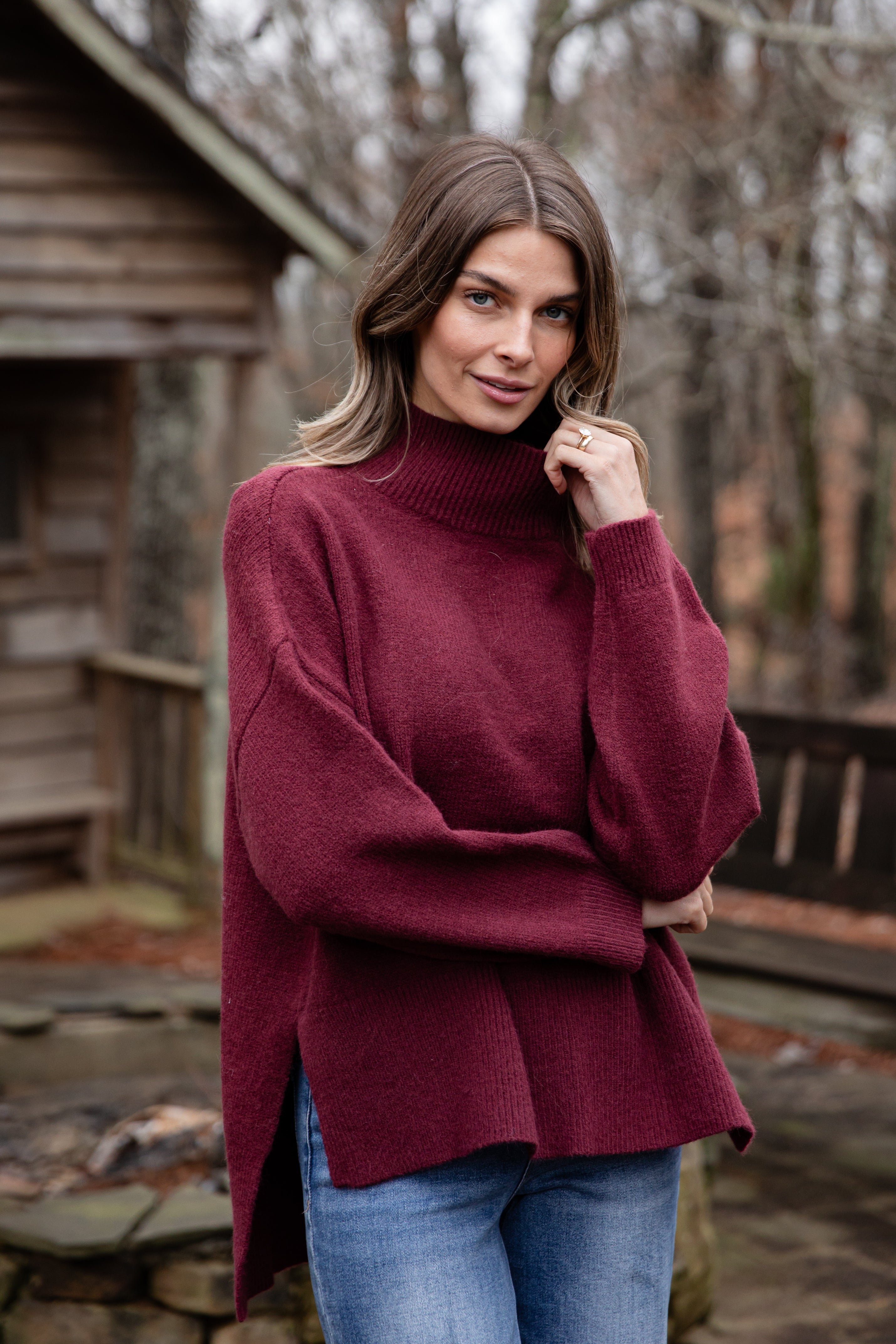Woman wearing a burgundy sweater and blue jeans standing outdoors.