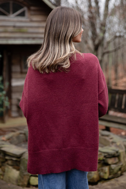 Person wearing a burgundy sweater standing outdoors with a rustic background