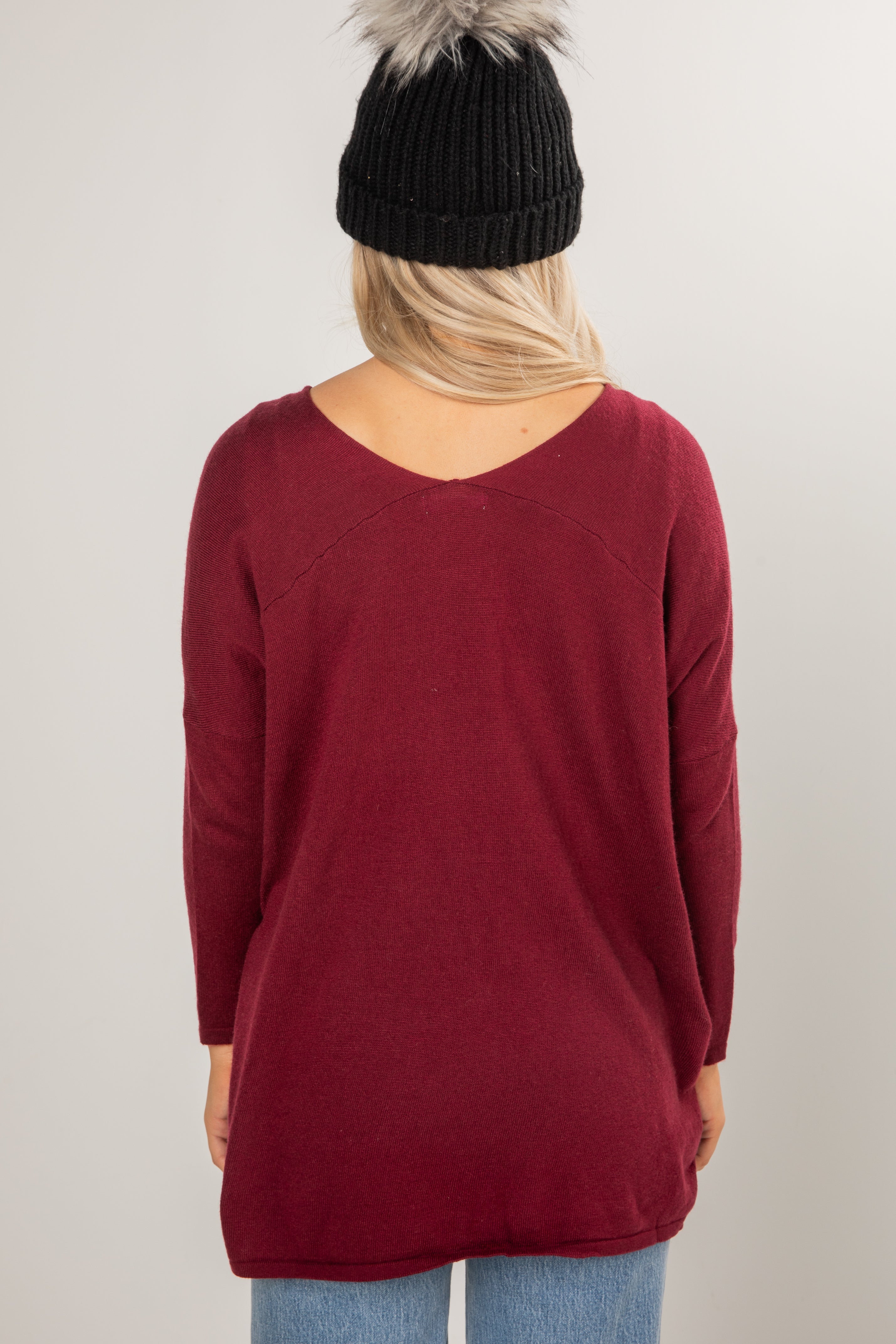 Person wearing a burgundy sweater and black beanie on a plain background