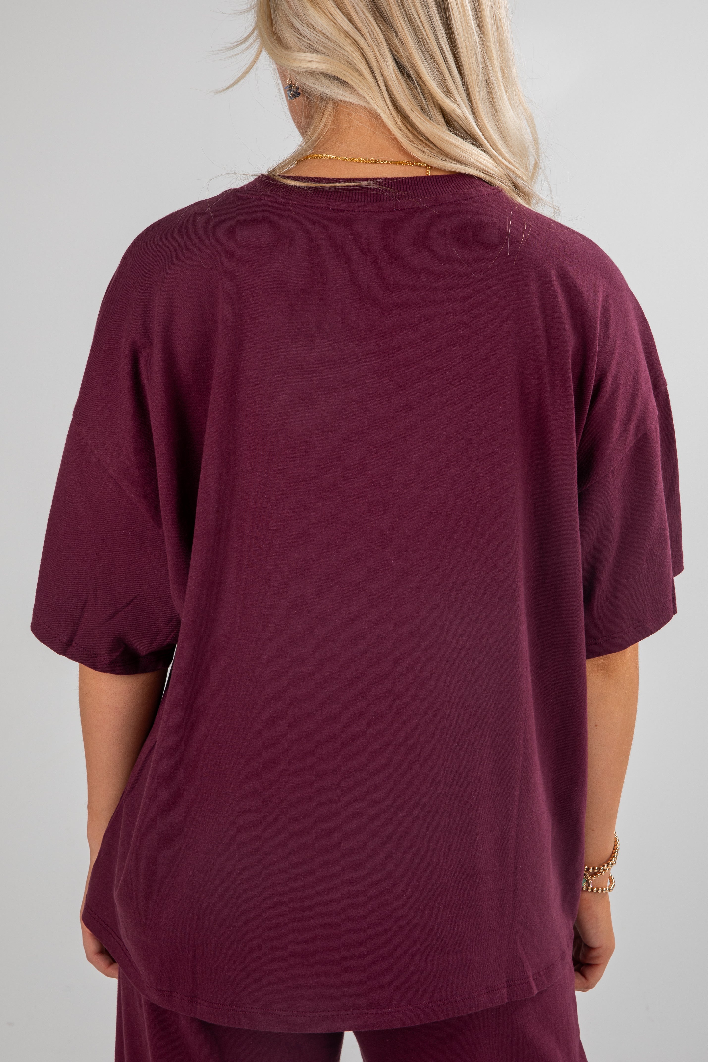 Person wearing a burgundy oversized t-shirt on a plain background