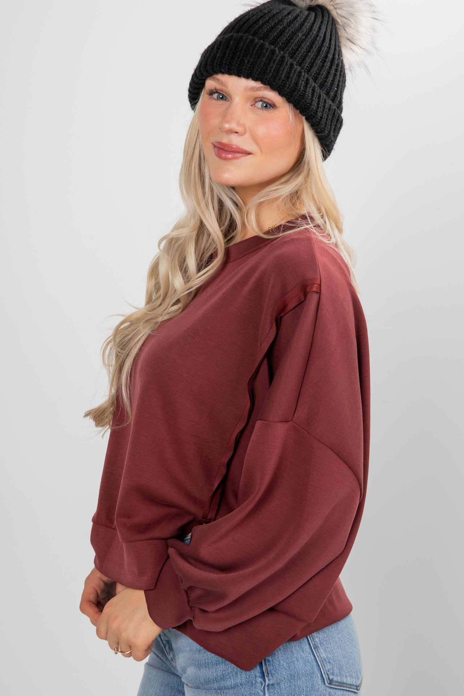 Woman wearing a maroon sweatshirt and black knit beanie on a white background