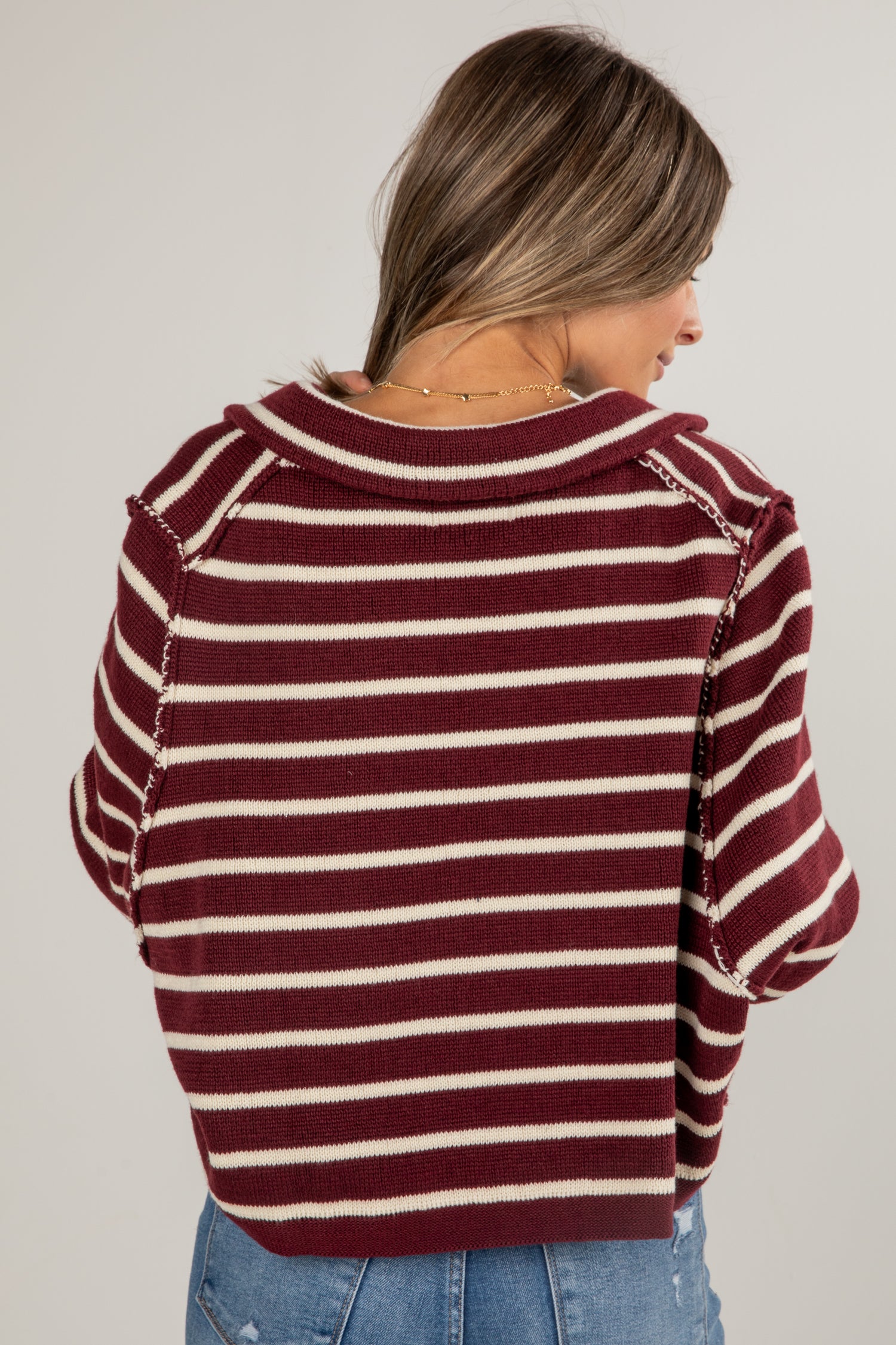 Woman wearing a maroon and white striped sweater on a plain background