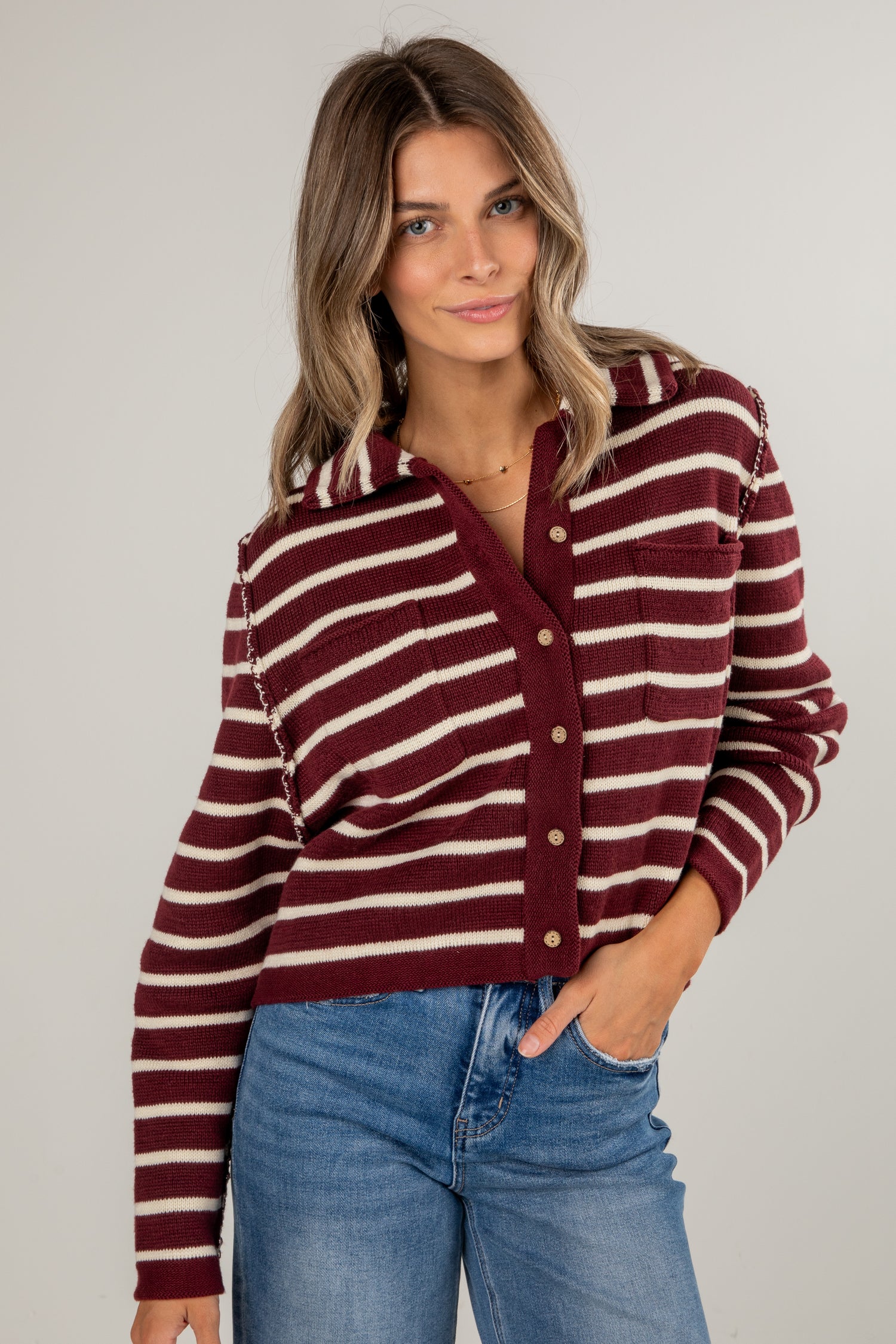 Woman wearing a maroon and white striped sweater with blue jeans on a plain background