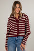 Woman wearing a maroon and beige striped sweater with blue jeans on a plain background